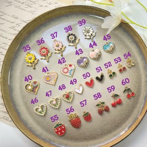 Puede incluir: Una colecci&oacute;n de peque&ntilde;os dijes decorativos en varias formas y colores, incluyendo flores, corazones, fresas y cerezas. Los dijes son dorados con detalles de esmalte y perlas, ideales para la creaci&oacute;n de joyas.