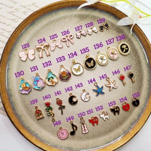May include: A collection of colorful enamel charms, including bows, butterflies, flowers, keys, and musical notes. The charms are arranged on a decorative plate, showcasing a variety of designs and colors.