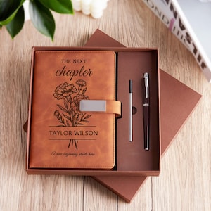 Può includere: Un set regalo con diario e penna in pelle marrone. Il diario è impresso con le parole "The Next Chapter", illustrazioni floreali e il nome "Taylor Wilson". Sono incluse una penna argentata e una penna nera.