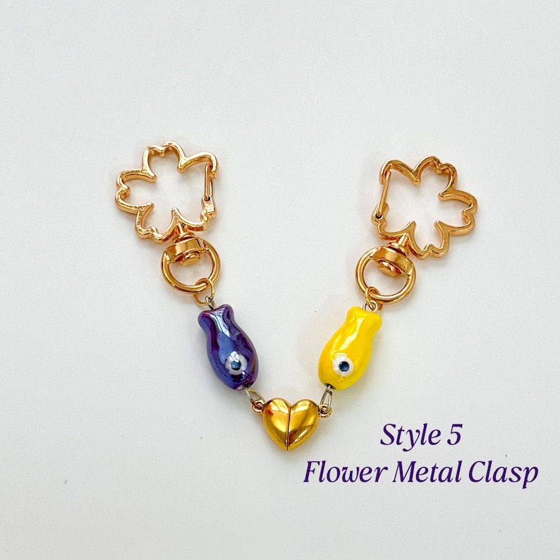 Op de afbeelding: Een goudkleurige metalen sluiting met een bloemdesign aan elk uiteinde, verbonden door een ketting. De ketting heeft een paarse en een gele tulpvormige bedel en een gouden hartbedel. De tekst "Style 5 Flower Metal Clasp" is zichtbaar.