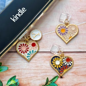 Könnte beinhalten: Herzförmige Anhänger mit Blumenmustern in Rot, Rosa, Blau und Gelb, mit goldfarbenen Rändern. Ein Anhänger hat einen weißen Kreis mit dem Buchstaben "Y". Das Wort "kindle" ist auf einem schwarzen Bildschirm zu sehen.