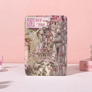 May include: A rectangular metal tin featuring a knight in silver armor standing next to a sword. The design includes a castle, pink flowers, butterflies, and the text "Once upon a time." The color palette consists of soft pinks, grays, and greens.