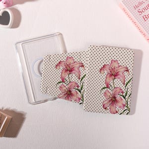 May include: A clear phone case and a matching phone wallet. The wallet features a cream background with black polka dots and pink lily flower illustrations. The phone case is transparent.