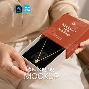 Peut inclure: Une boîte à collier coulissante rectangulaire avec un étui extérieur couleur terre cuite portant le texte blanc Necklace Box Mockup et un plateau intérieur blanc contenant un collier à chaîne dorée avec un petit pendentif rond sur un insert en velours noir.