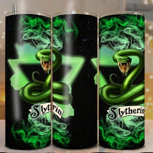 Peut inclure: Un gobelet en acier inoxydable avec un serpent vert à gueule ouverte, sur fond noir avec de la fumée verte et un triangle vert. Le mot "Slytherin" est affiché sur une bannière.