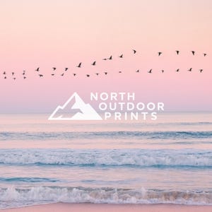 May include: A serene coastal scene with a pink and peach sky, gentle waves, and a sandy beach. Silhouetted birds fly across the sky. The white logo for "NORTH OUTDOOR PRINTS" is centered in the image.