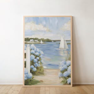 May include: A framed painting depicts a coastal scene with sailboats on the water. Blue hydrangeas frame a path leading to the beach. The sky is a mix of blue and white, with a light wooden frame.