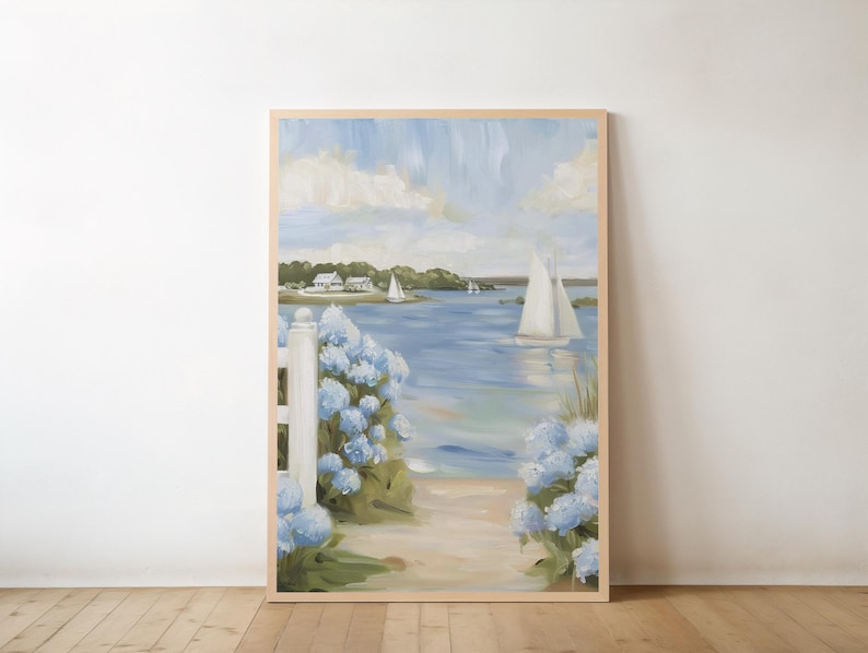 May include: A framed painting depicts a coastal scene with sailboats on the water. Blue hydrangeas frame a path leading to the beach. The sky is a mix of blue and white, with a light wooden frame.