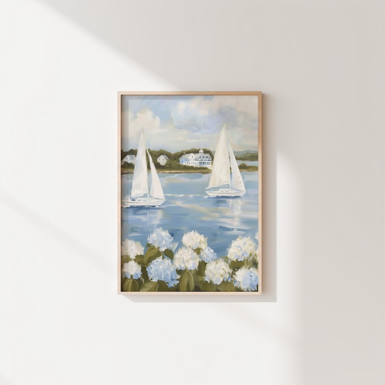 May include: A framed painting depicts two sailboats on a blue body of water, with white hydrangeas in the foreground. The sky is a mix of blue and white, and a white building is visible in the distance.