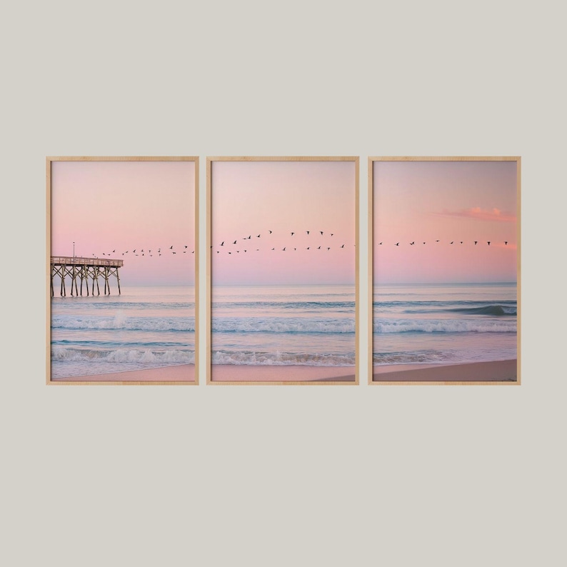 Pastel coastal scene with birds flying across a pink sunrise sky, wooden pier on the left, and gentle ocean waves meeting a soft sandy shore - peaceful and minimal wall art.