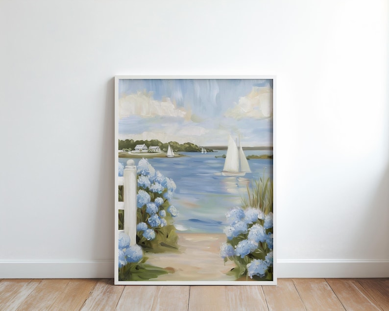 May include: Framed painting of a coastal scene with sailboats on the water. The artwork features a white picket fence, blue hydrangeas, and a sandy path leading to the water. The sky is a light blue with fluffy white clouds.