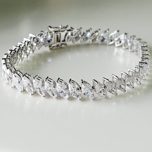 May include: A silver bracelet with a series of marquise-cut, clear gemstones. The bracelet features a secure clasp and is designed with a repeating pattern of the gemstones. The gemstones are set in a silver metal setting.