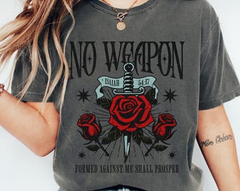 Puede incluir: Camiseta gris oscuro con un diseño gráfico que presenta el texto "NO WEAPON" sobre una espada que atraviesa una rosa roja, con el texto "FORMED AGAINST ME SHALL PROSPER" debajo. La camiseta también tiene el texto "ISAIAH 54:17".