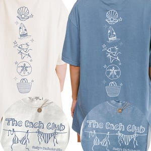 May include: Two oversized t-shirts, one cream and one blue, featuring a vertical line of beach-themed illustrations in white. The shirts have the text "The Bach Club" and "Emily's Bachelorette 2024" printed on the front.