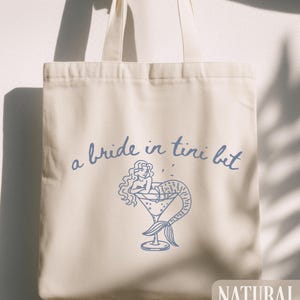 May include: A white ceramic mug with a black handle and the text "But First, Coffee" in a handwritten style. The mug is on a white surface. The mug is likely for hot beverages.