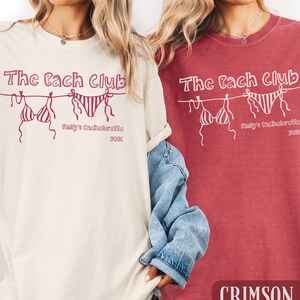 May include: Two t-shirts, one cream and one crimson, with the text "The Bach Club" and a bikini graphic. Below the graphic is "Emily's Bachelorette 2026". The crimson shirt has the word "CRIMSON" at the bottom.