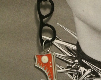 May include: A single silver earring with a black glasses frame and a red and white sneaker charm. The sneaker charm has a white toe cap and a white circle. The earring hangs from a silver hook.