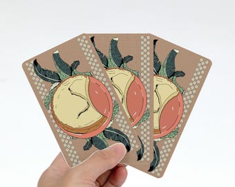 May include: Three rectangular playing cards with a tan background featuring a central illustration of a sliced peach surrounded by dark green tropical leaves. Each card has a vertical border of small white circles along the left and right edges.