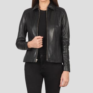 May include: Black leather jacket with a collared neckline and a zipper closure. The jacket has long sleeves and a tailored fit. The model is wearing black pants and a black top. The jacket is a classic style.