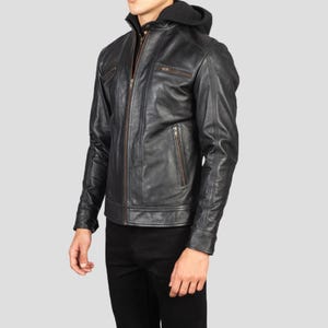 May include: Black leather jacket with a zip-up front, multiple pockets, and a hooded sweatshirt lining. The jacket has a classic biker style with a tailored fit. The jacket is worn with black pants.