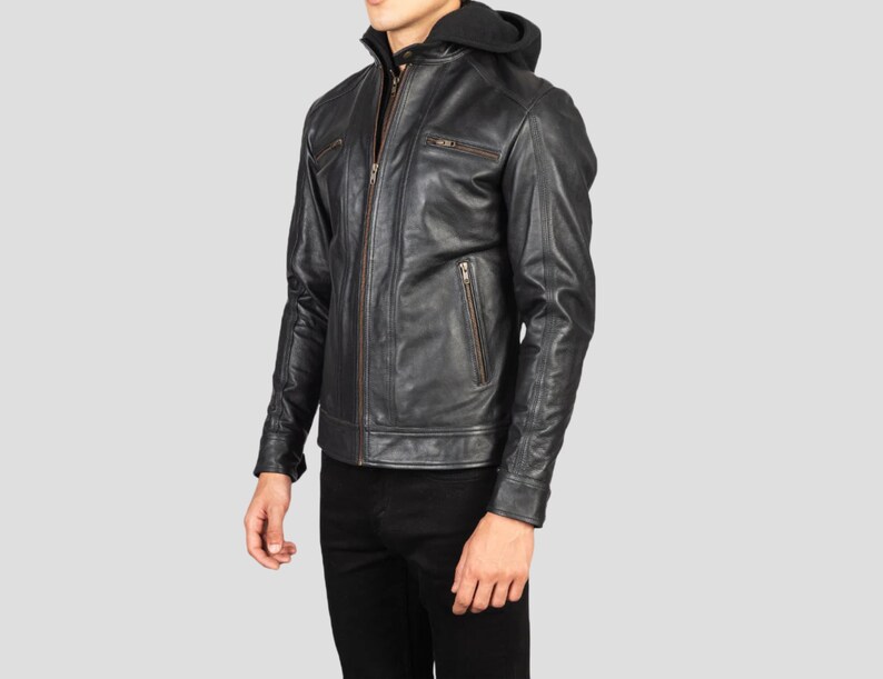 May include: Black leather jacket with a zip-up front, multiple pockets, and a hooded sweatshirt lining. The jacket has a classic biker style with a tailored fit. The jacket is worn with black pants.