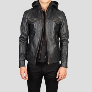 May include: Black leather jacket with a hood and a zip-up front. The jacket has two chest pockets with zippers and a slim fit. The model is wearing black pants and a black shirt underneath the jacket.