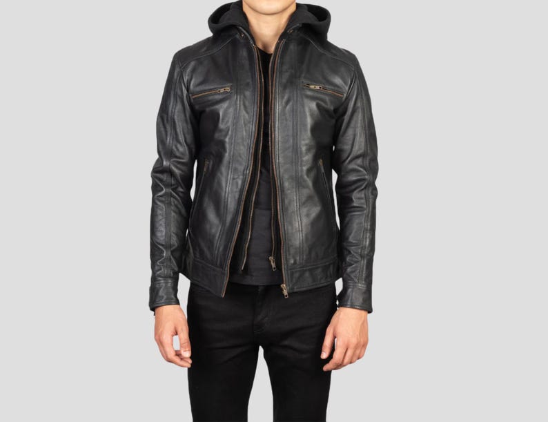 May include: Black leather jacket with a hood and a zip-up front. The jacket has two chest pockets with zippers and a slim fit. The model is wearing black pants and a black shirt underneath the jacket.