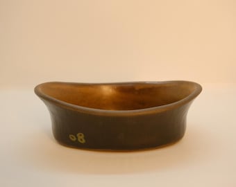 May include: A handcrafted, oval-shaped ceramic bowl with a dark brown exterior and a lighter brown interior. The bowl has a textured surface and the number "08" is visible on the side. This decorative bowl is suitable for serving or display.