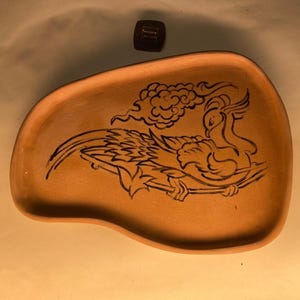 May include: A terracotta tray with a black and white design of a bird with its wings spread. The bird is surrounded by clouds.
