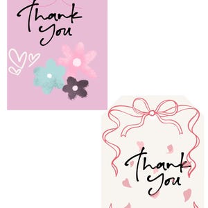 Op de afbeelding: Twee cadeaulabels met de woorden "Bedankt" in handschrift. E&eacute;n label is roze met bloemen en een vlinder. Het andere is gebroken wit met roze strikken en vallende bloemblaadjes. Beide labels hebben een gaatje aan de bovenkant.