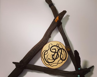 May include: A rustic, triangular wall hanging crafted from dark brown branches. A circular wooden slice in the center features a black snake design. Amber-colored stones and decorative beads add detail to this unique piece.