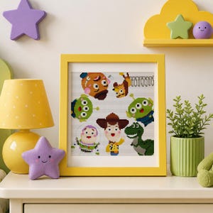 May include: A square yellow frame containing a pixel art cross-stitch pattern featuring various animated characters including a cowboy, a space ranger, a green dinosaur, and two three-eyed aliens arranged on a white background.