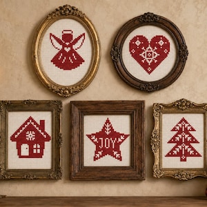 May include: Five framed cross-stitch artworks featuring red holiday motifs on white fabric. The designs include an angel, a heart, a house, a star with the text JOY, and a Christmas tree. Each piece is displayed in an ornate, vintage-style frame.
