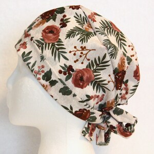 May include: A white scrub hat with a floral print featuring red roses, green leaves, and brown berries.