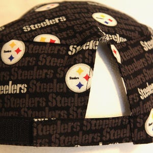 May include: Black and gray baseball cap with the word "Steelers" repeated in a pattern. The cap has a black adjustable strap and a black and yellow logo with the word "Steelers" on it.
