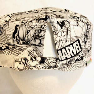 May include: A white and black Marvel comic book print scrub cap. The cap features a hook and loop closure and is designed to fit comfortably. The Marvel logo is prominently displayed on the side of the cap.
