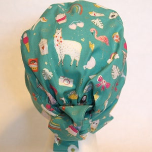 May include: A teal blue scrub hat with a colorful print featuring llamas, flamingos, ice cream cones, and other fun designs. The hat is tied at the back with a bow.