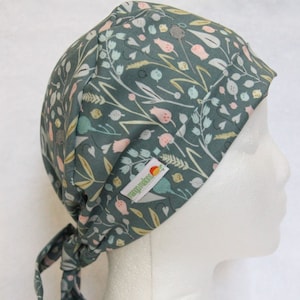 May include: A teal blue scrub hat with a floral pattern featuring pink, white, and yellow flowers. The hat has a tie at the back and a small label that says "Happy Scrubs".