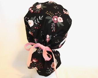 May include: Black scrub hat with a floral print featuring pink, burgundy, and white flowers on a black background. The hat has a pink ribbon tie.