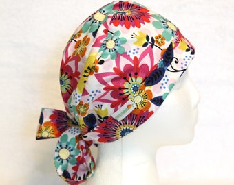 May include: A white scrub hat with a colorful floral print. The hat has a tie at the back and a small logo on the side.