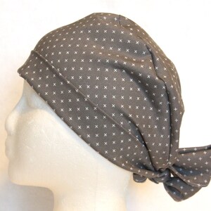 May include: A gray scrub hat with a white cross pattern. The hat has a tie at the back.