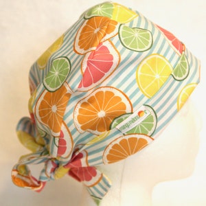 May include: A white scrub hat with blue stripes and a colorful citrus fruit print. The hat has a tie on the back and the text "mango mambo" is visible on the front.