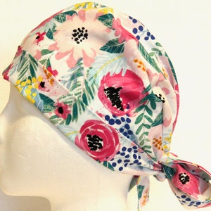 May include: A white scrub hat with a floral print featuring pink, blue, and green flowers. The hat has a tie at the back.