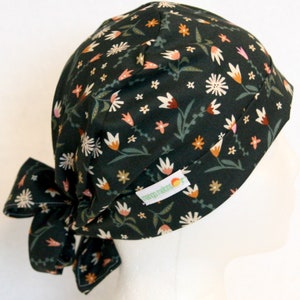 May include: A dark green scrub hat with a floral print featuring white, pink, and orange flowers. The hat has a tie at the back and a small label that says "nap-time".