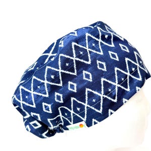 May include: A navy blue scrub cap with a white geometric diamond pattern. The cap is made of a soft, possibly satin-like fabric. The cap is designed to cover the head and hair, often used in medical or surgical settings.