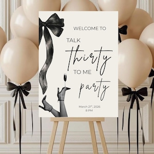 以下が含まれることがあります： 「Welcome to Talk Thirty to Me Party」の文字が入った、木製のイーゼルに立てられたパーティーサイン。黒いリボンと、シャンパングラスを持つ女性の腕の白黒イラストで飾られています。ベージュの風船と黒いリボンが背景にあります。