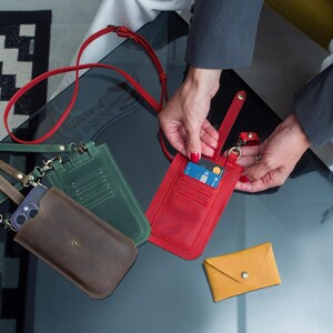 Puede incluir: Una colecci&oacute;n de fundas de tel&eacute;fono de cuero y carteras peque&ntilde;as en varios colores. Las fundas son marrones, verdes y rojas, con una cartera amarilla. La funda roja tiene una tarjeta de cr&eacute;dito. Todas tienen correas.