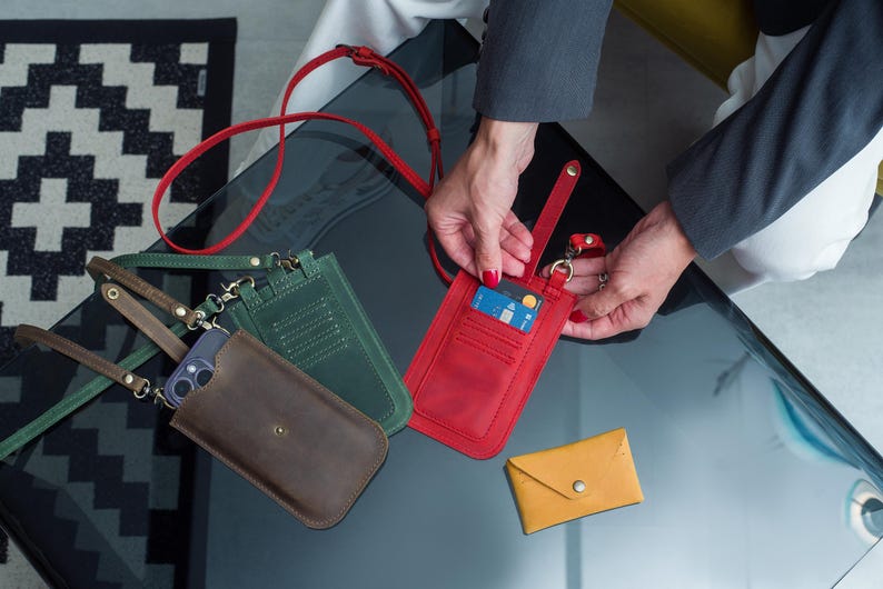 Puede incluir: Una colecci&oacute;n de fundas de tel&eacute;fono de cuero y carteras peque&ntilde;as en varios colores. Las fundas son marrones, verdes y rojas, con una cartera amarilla. La funda roja tiene una tarjeta de cr&eacute;dito. Todas tienen correas.