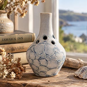 May include: A ceramic bud vase with a narrow neck and a bulbous body featuring a textured surface with blue circular patterns. The upper section of the vase has several small circular openings arranged around the neck for individual flower stems.