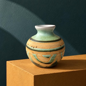 May include: A round ceramic vase with a narrow neck and a wide body. The vase features a gradient of colors including a white rim, a light green upper section, and a tan lower section with dark green horizontal bands and abstract curved patterns.